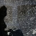 A classical statue silhouetted against glittering, backlit fountain spray