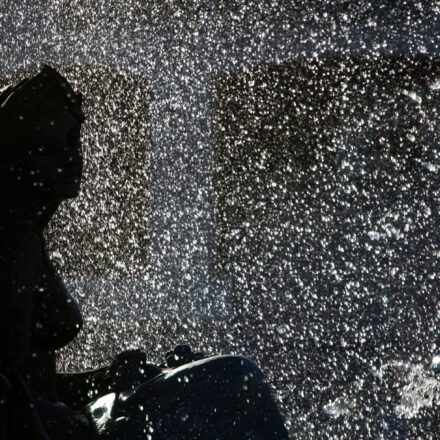 A classical statue silhouetted against glittering, backlit fountain spray