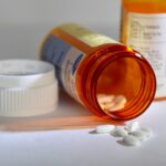 A pill container lies on its side with white pills spilling out