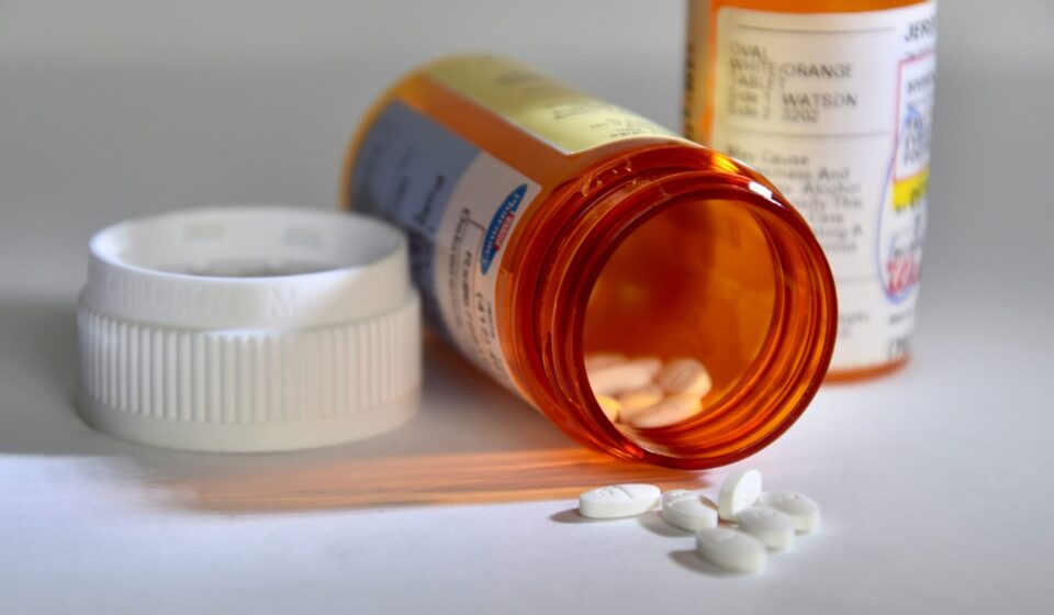 A pill container lies on its side with white pills spilling out