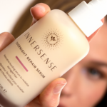 A woman holds a bottle of Innersense Overnight Repair Serum close to the camera, with her face softly blurred in the background.